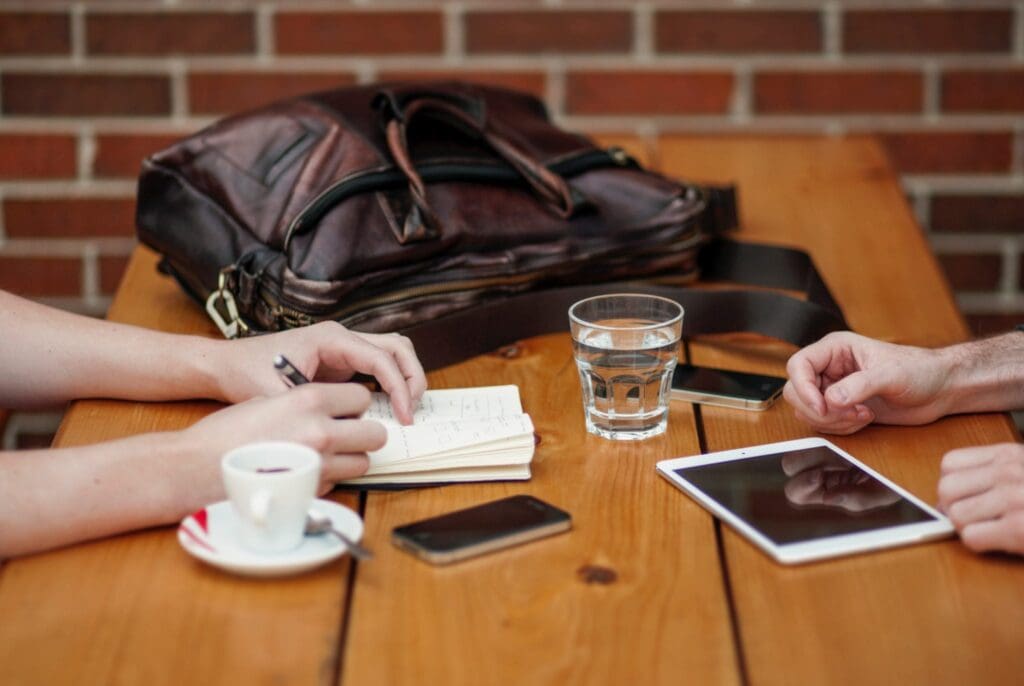 Two people sitting at wooden table with iphones and ipad, coffee and water.